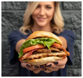 A woman holds out a large, stacked burger with lettuce, tomato, and bacon from Mr MIKES Steakhouse.