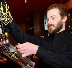 A bartender at Mr MIKES Steakhouse pours a beer from a Big Horn Lager tap, focusing intently as he fills a glass.