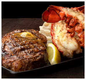 A plate of Mr MIKES Steakhouse’s steak and lobster, served with mashed potatoes and a lemon wedge.