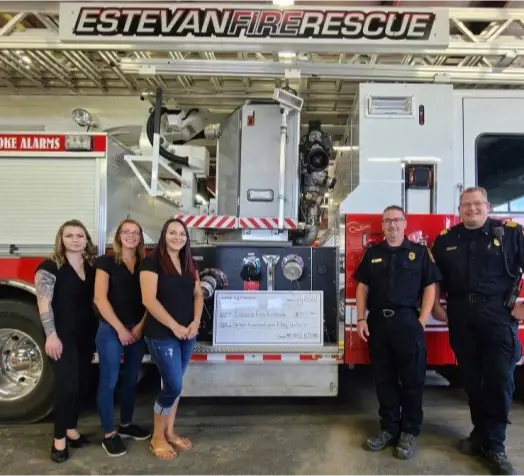 A group of people stand in front of an Estevan Fire Rescue truck, holding a large check for a donation to the fire department.